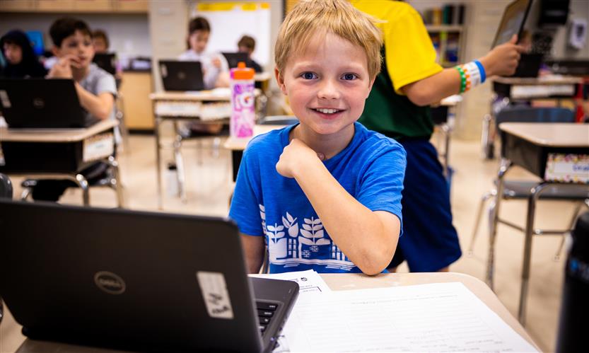 A blond boy wearing a blue t shirt uses a Chromebook